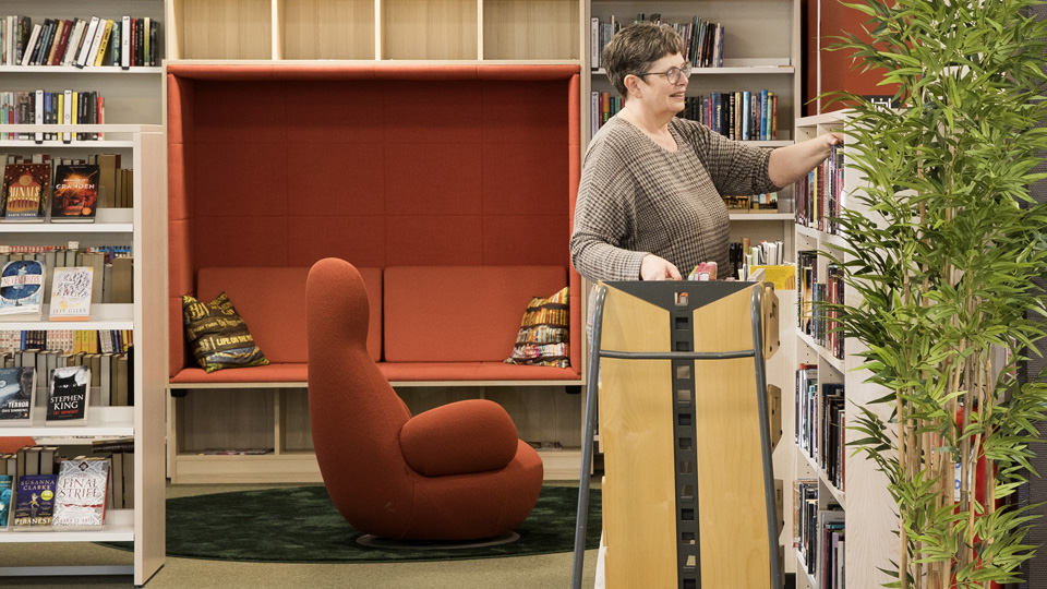 En bibliotekarie ställer upp böcker i hyllan på Vänersborgs bibliotek.