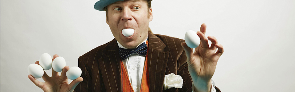 En man med hatt och kavaj trollar fram ägg ur munnen.