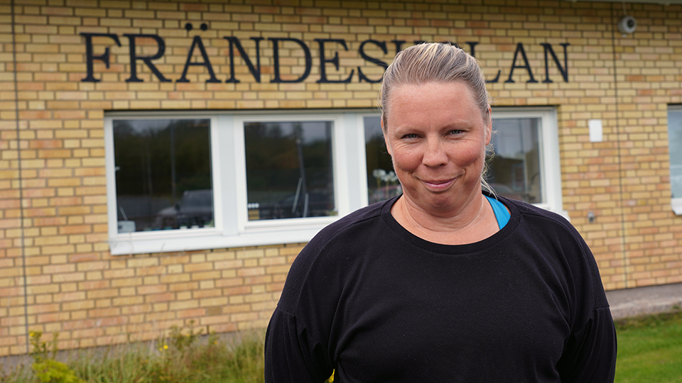 En kvinna i svart tröja och med hästsvans står framför en tegelbyggnad med texten Frändeskolan