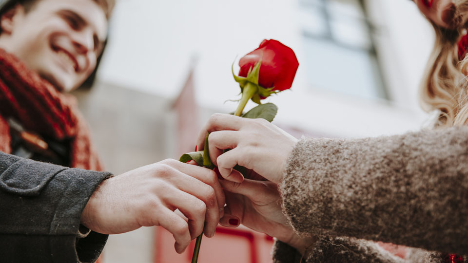 En glad kille räcker över en röd ros till en tjej.