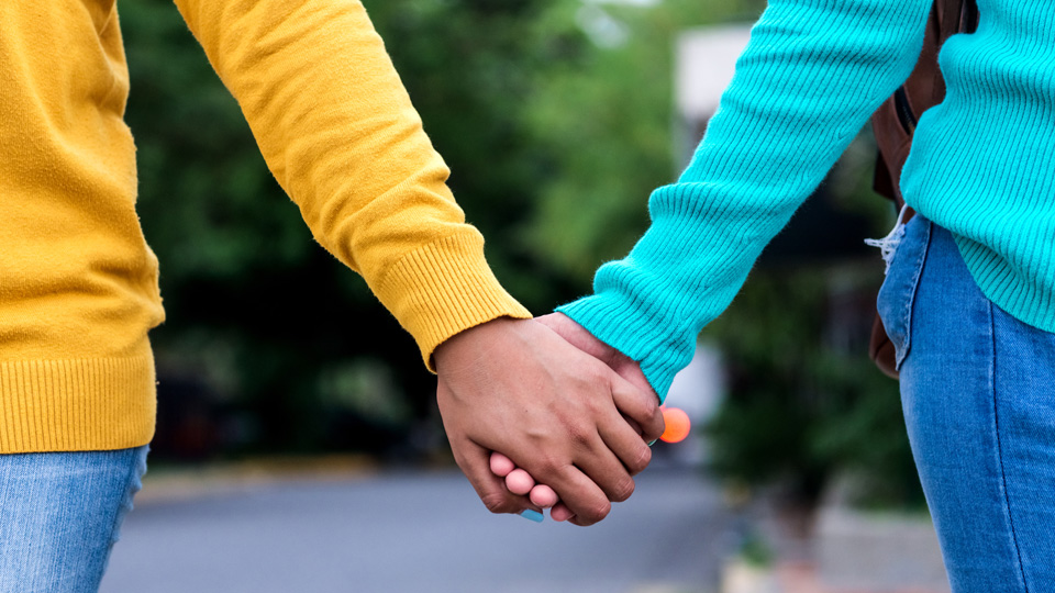 Två unga personer i färgglada tröjor håller varandra i handen.