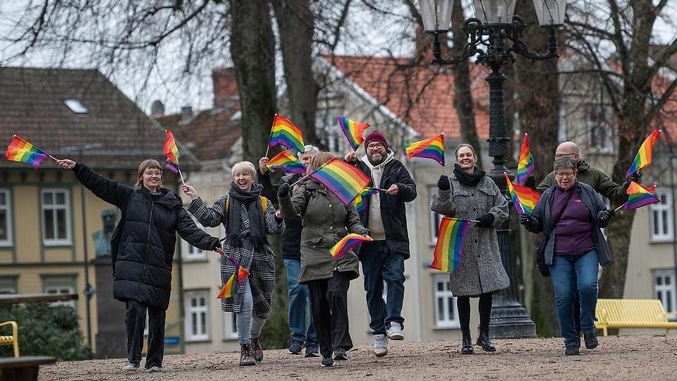 Ett gäng glada personer springer genom Plantaget i Vänersborg med regnbågsflaggor i händerna.