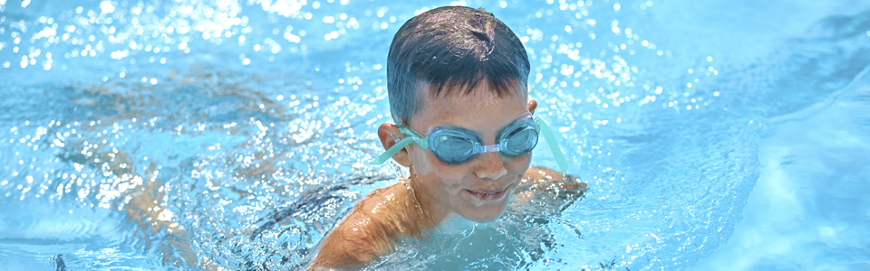 Pojke med simglasögon simmar i en bassäng.