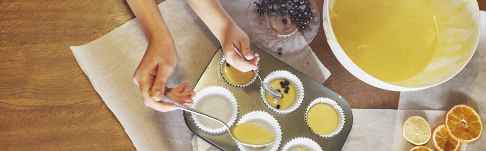 Händer som häller smet i muffinsformar.