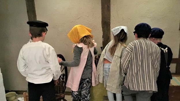 Bilden visar barn  som klätt ut sig i gammaldags kläder (bilden är tagen bakifrån)