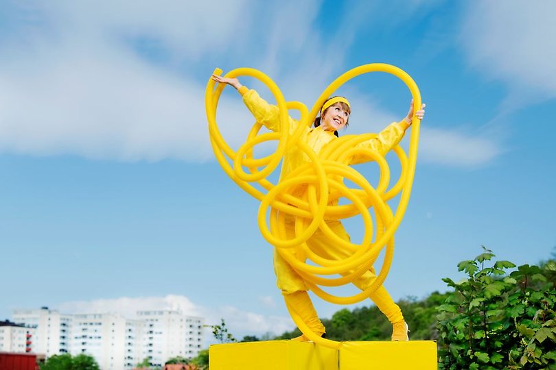 En kvinna klädd i gult med gula plaströr mot en blå himmel i bakgrunden.
