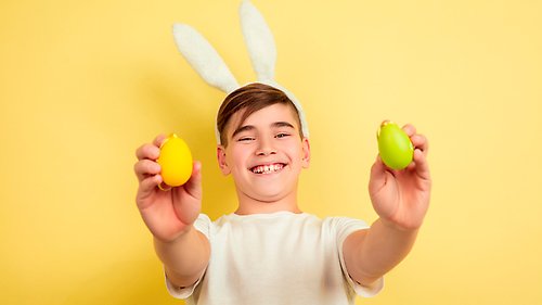 Ung kille med kaninöron på huvudet sträcker fram två färgglada ägg.