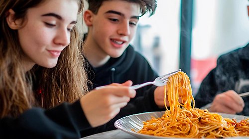 Två tonåringar äter spagetti.