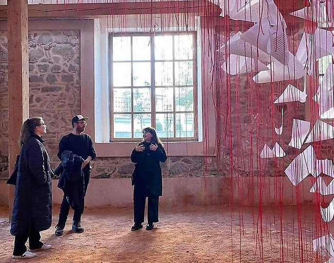 Konstvisning i Pristina med ett hängande konstverk från av röda trådar golv till tak i förgrunden.