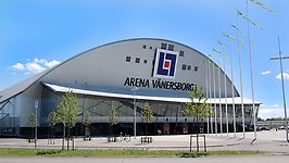 Arena Vänersborg från håll mot en blå himmel och sverigevimplar på flaggstängerna. 
